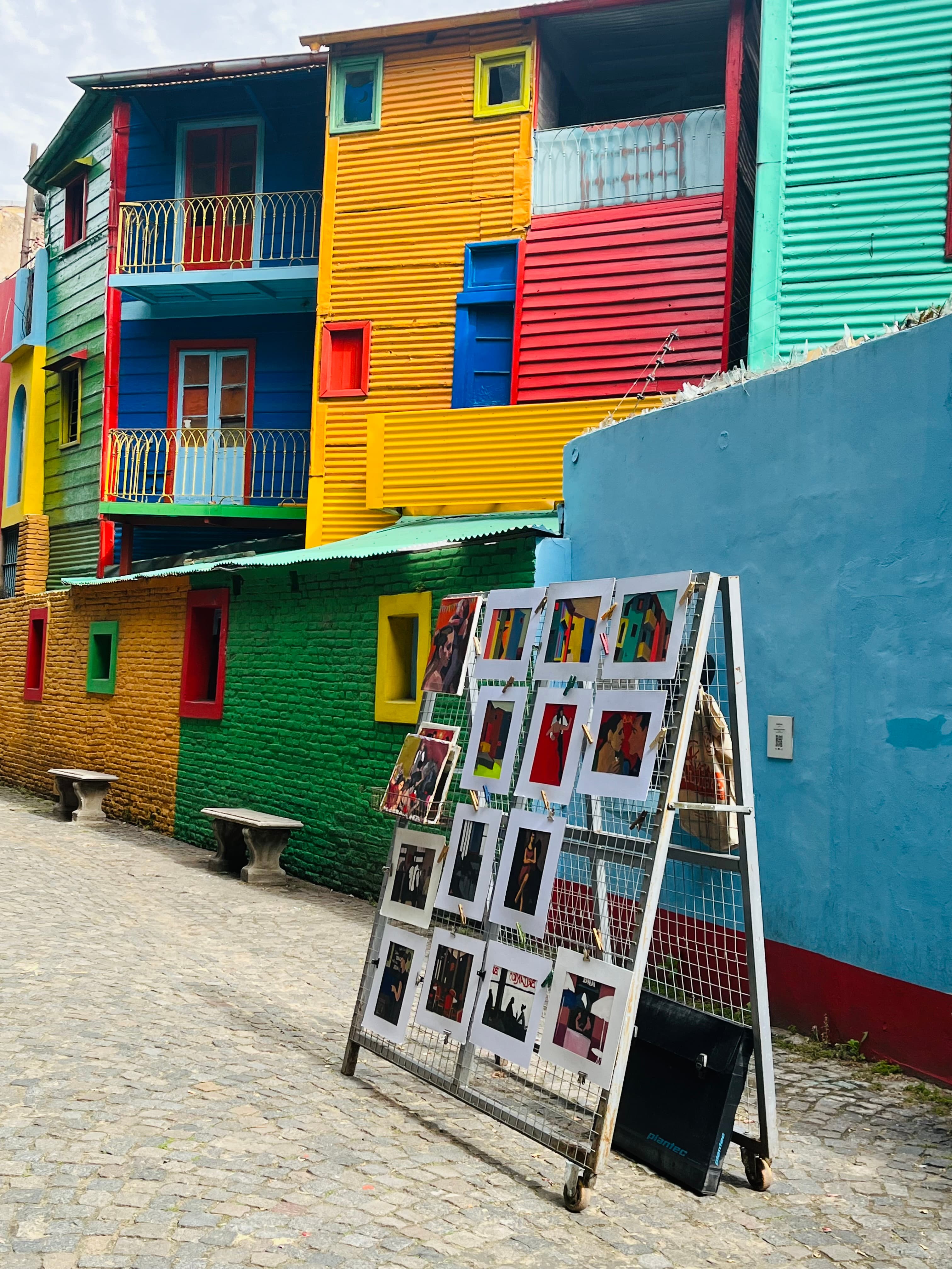 Casas de chapa colorida e rua de paralelepípedo no Caminito, bairro de La Boca em Buenos Aires, com uma banca de quadros de artista local